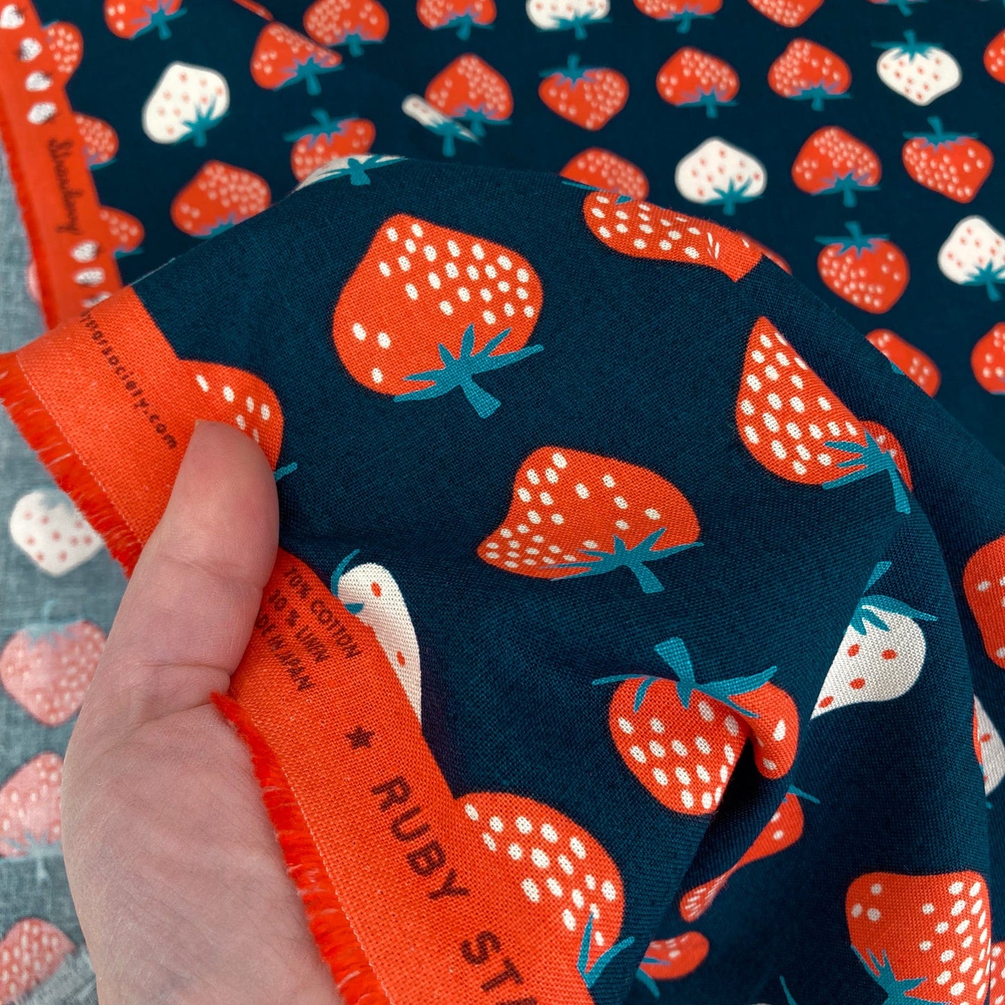 Fabric with strawberry pattern held by a hand, with 'Ruby Star' label visible.