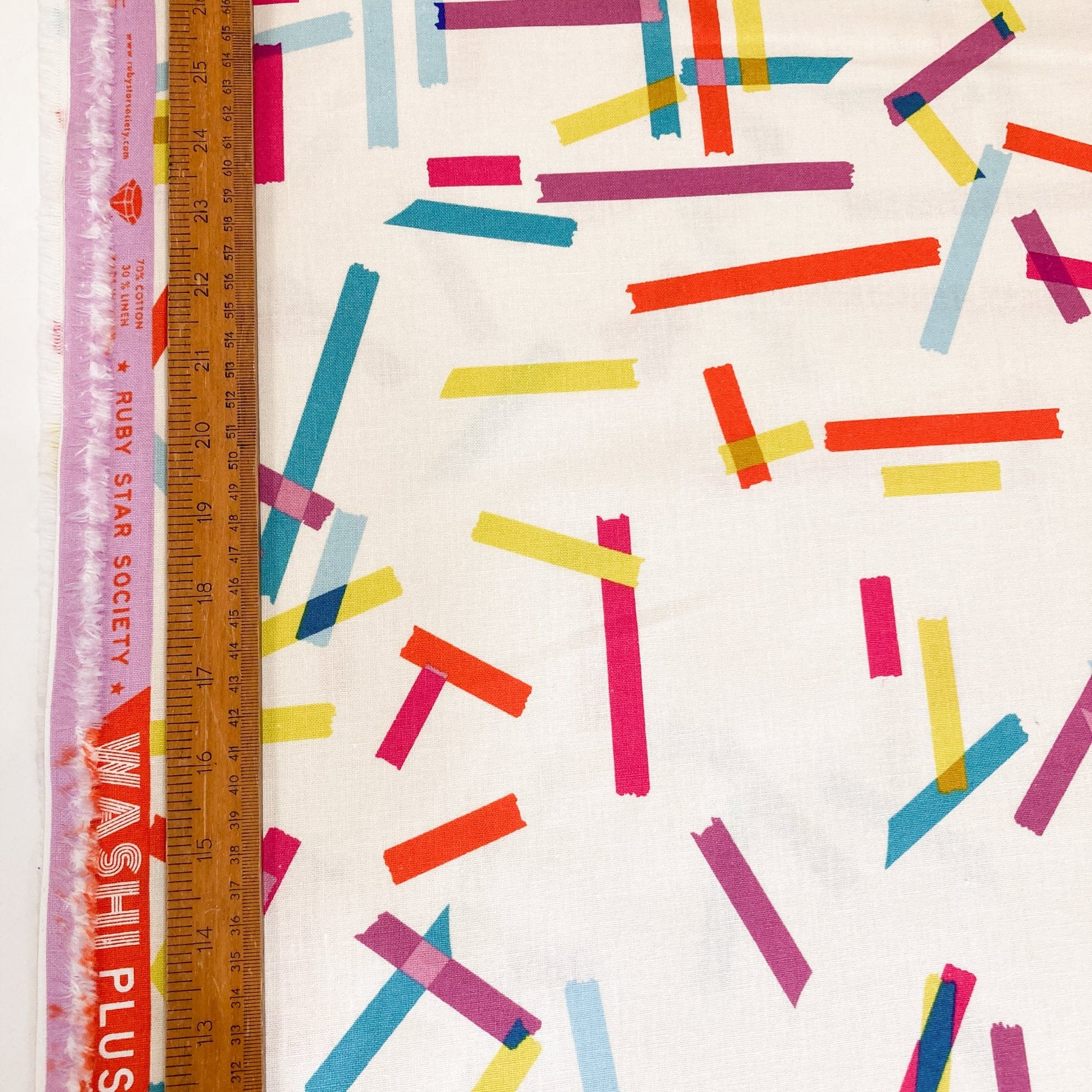 Cream cotton & linen canvas fabric with washi tape print in bright colours with a ruler for scale.