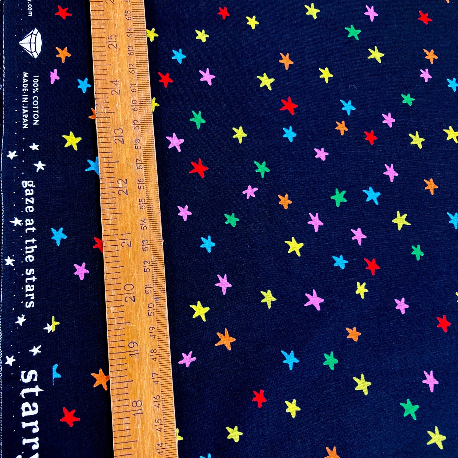 Black quilting cotton with colorful star pattern and a wooden ruler for scale.