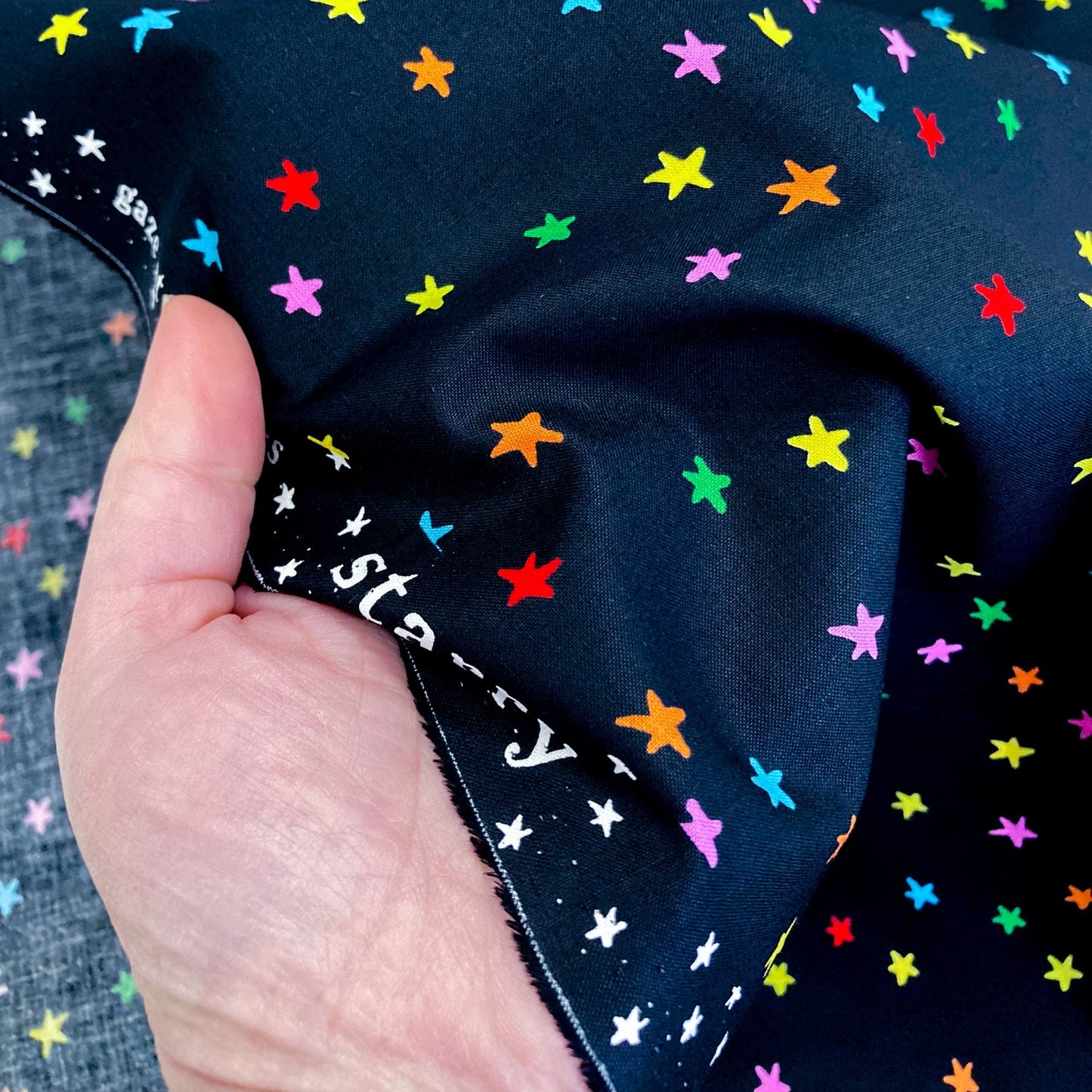 Black quilting cotton with colorful star pattern held by a hand