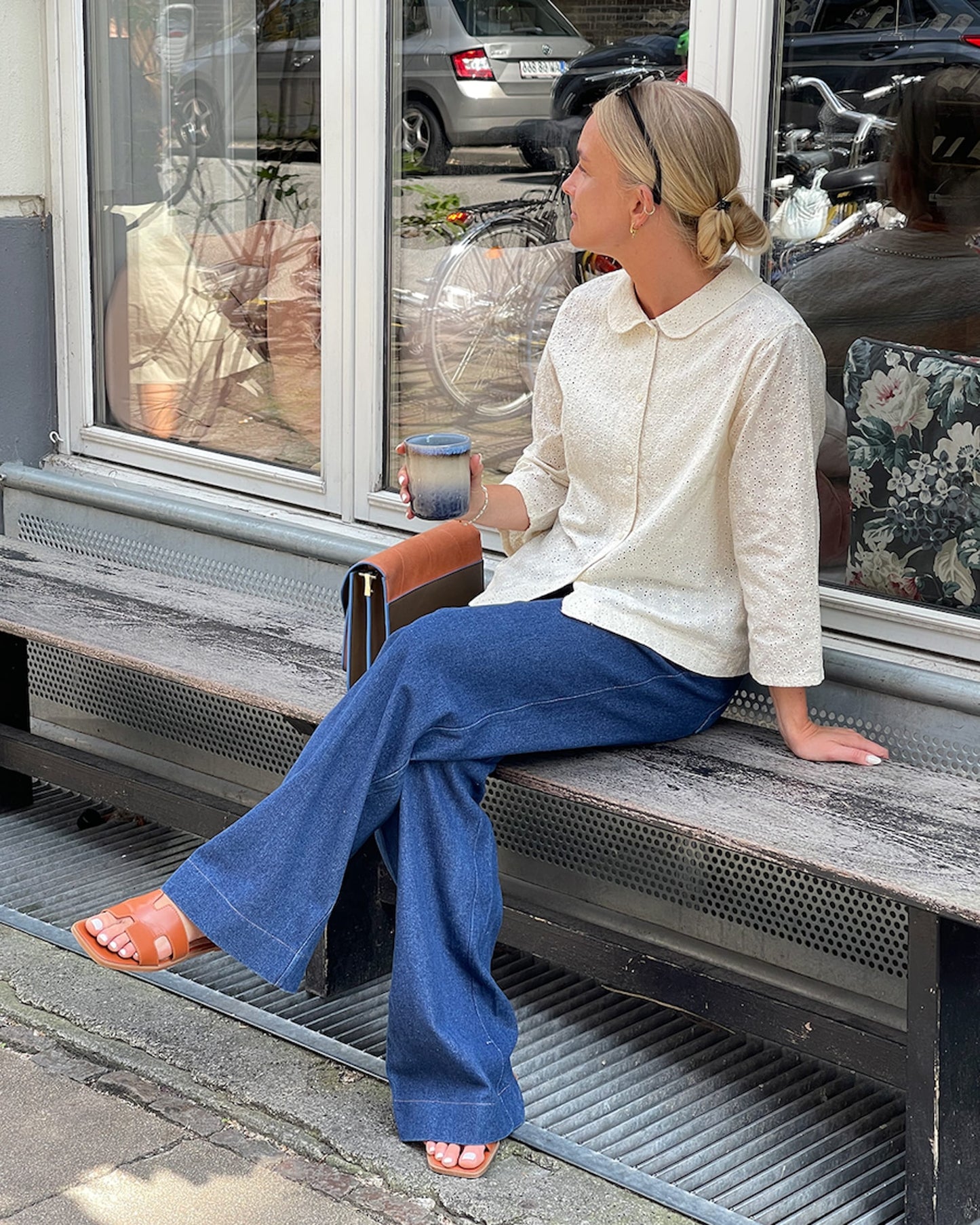 Woman sitting on a bench outside a store, holding a coffee cup.